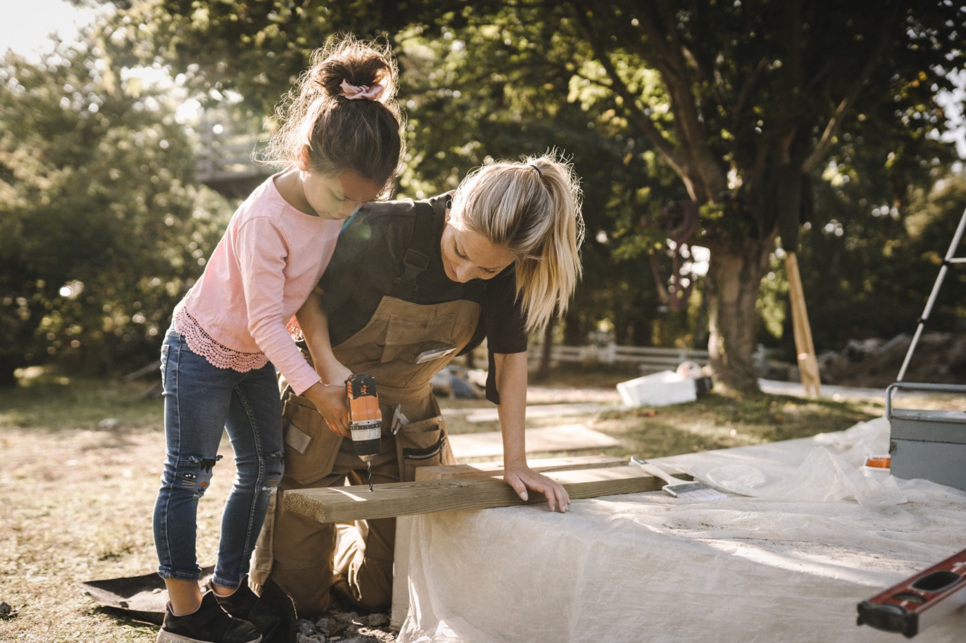 En mor som snekrer ute i hagen med datter ved siden av